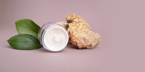 Open cosmetics container with white cream and glossy green leafs on background,eco friendly concept.Large banner with negative space.