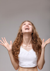 an emotional curly-haired woman in a white T-shirt shouts loudly, gesturing with her hands while standing on a gray background