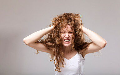 a woman with long curly hair screams loudly, tangled in them and holding her head