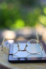 Fototapeta na wymiar E-book reader and reading glasses in the garden. Selective focus.