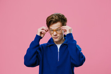 a young man with a beautiful hairstyle in a blue sweater adjusts his glasses