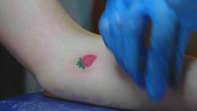 A close-up view of a professional woman tattooist who is tattooing on the leg of a young girl. Hands of a tattooist. Tattooist makes a tattoo.