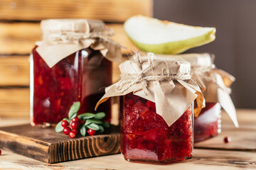 Jars of homemade lingonberry and pear jam with craft paper on lids on wooden surface next to fresh...