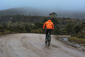 Cyclist man with orange reflective jacket riding mountain bike on a off road path in the mountains....