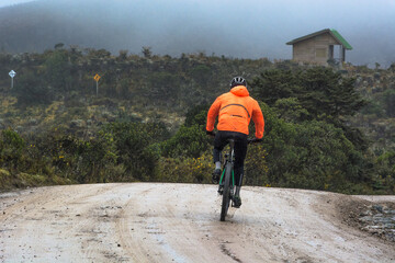 Cyclist man with orange reflective jacket riding mountain bike on a off road path in the mountains....
