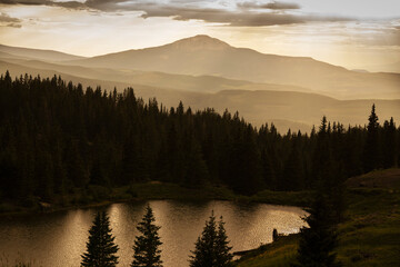 Fototapeta na wymiar USA, Colorado, Uncompahgre National Forest. Sunset silhouettes over mountain forest and lake.