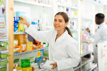 Portrait of a young female pharmacist laying out goods on the shelves of a rack in a pharmacy