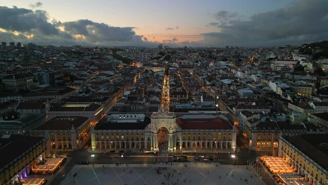Aerial hyper lapse view of Lisbon, Portugal, flying backward over historic landmark Rua Augusta Arch and Comercio Square at dusk.