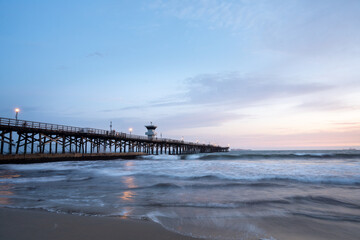 Fototapeta premium Crescent Moon Glows Over Seal Beach Pier after Sunset long exposure waves