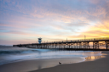 Fototapeta premium Vibrant Sunset burns over Seal Beach Pier Long Exposure Wave Photography 