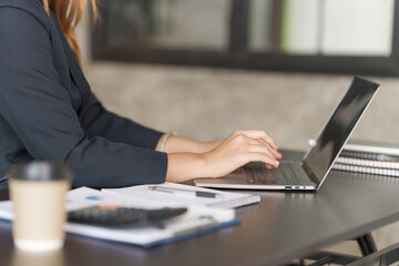 Using laptop, Young pretty asian stock manager checking list of product and working at workstation.