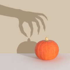 Halloween minimal concept with pumpkin and witch or zombie hand shadow. Creative spooky holiday fun background