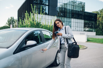 Business woman getting into the car and using smartphone - Powered by Adobe