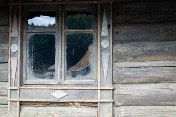 The facade of an old wooden log building with a small window divided into 4 parts