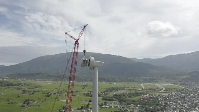 Aerial footage of wind turbine tower installation by big red crane. Clean alternative energy concept to reduce global warming and climate change for sustainable growth and development.