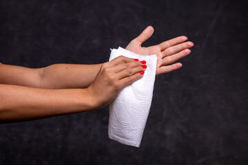 Woman cleaning her hands with white soft tissue paper, dark background