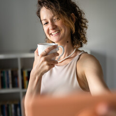 One woman standing in the office drinking coffee and make video call