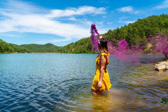 Young woman in forest having fun with purple smoke grenade, bomb
