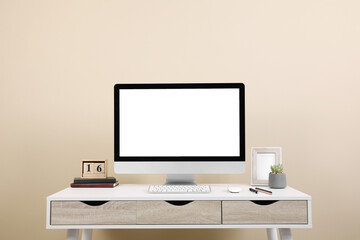 Comfortable workplace with blank computer display on desk near beige wall. Space for text