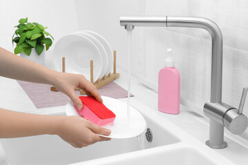 Woman washing plate above sink in kitchen, closeup