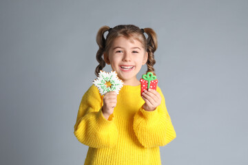 Cute little girl with Christmas gingerbread cookies on light grey background