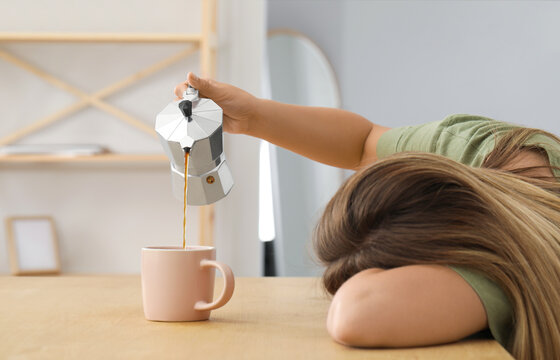 Sleepy woman pouring coffee into cup at wooden table indoors