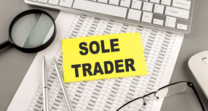 SOLE TRADER text on yellow sticky on clipboard with chart, wooden background