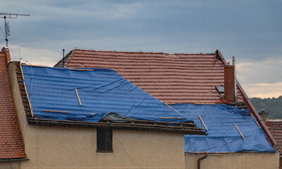 The protective tarpaulin on the roof at the storm with rain. The tarp covers the roof of the old house in the reconstruction. - obrazy, fototapety, plakaty