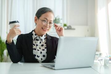 Successful senior female entrepreneur wearing glasses checking online news or email on her laptop.