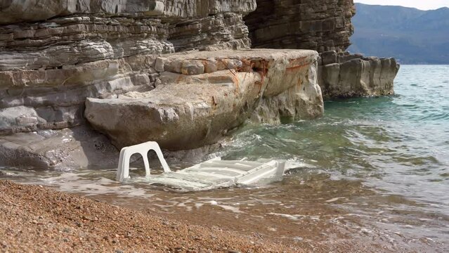 Old sunbed is washed ashore by wave. Plastic pollution after storm on wild beach. Traces of civilization, consumer attitudes, environmental pollution. End of tourist season, closed beach with trash.