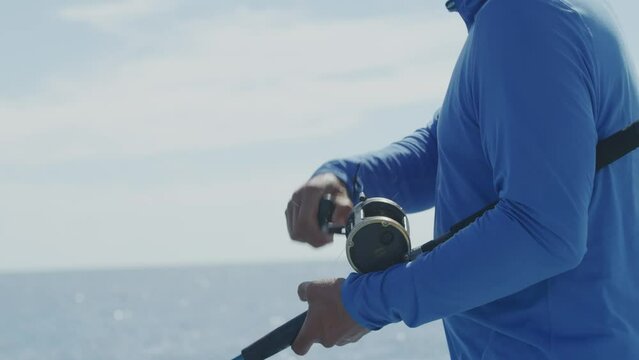 Close up unrecognizable man spinning fishing reel with blue ocean backdrop on small fishing boat in Mexico