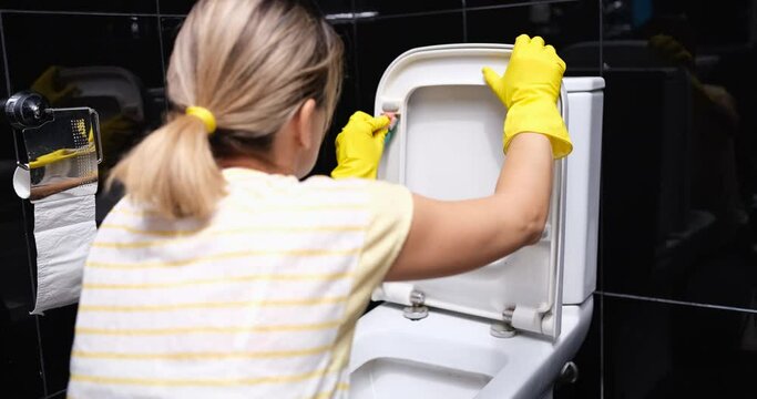 Hands in yellow rubber gloves wash toilet seat in toilet with sponge