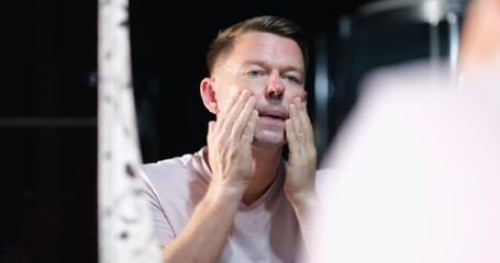 Young man shaves in bathroom and applies aftershave lotion to face