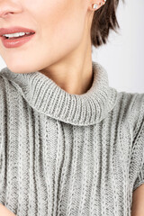 Studio portrait of beautiful and sexy woman with beautiful body shape wearing gray sweater without sleeves. Visible bare hands and chin of model. Selective focus and image with shallow depth of field