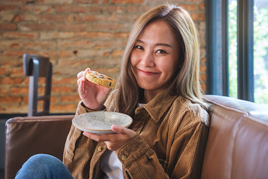 Portrait image of a beautiful young asian woman holding and eating a piece of cookie