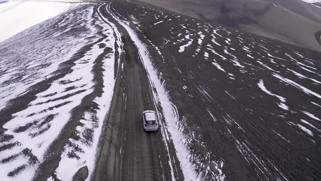 Imagen aerea desde dron de una camioneta de color plateado viajando por un camino montañoso con nieve