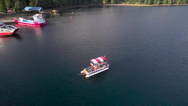 Peque&ntilde;a embarcaci&oacute;n detenida en un lago. Se ve el puerto con 2 embarcaciones tipo barcaza o ferry 