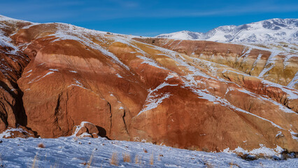 Fototapeta na wymiar Bright unusual red-orange hillsides and mountain range against the blue sky. Dry grass in a snowy valley. Altai Mars Kyzyl Chin