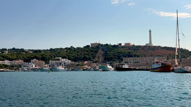 Santa Maria di Leuca city and harbor in Salento with iconic lighthouse and moored ships seen from navigating touristic boat, Apulia in southern Italy. Low angle water surface pov