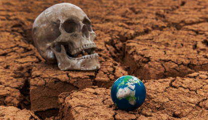 A miniature globe and a human skull against the background of cracked dry clay in the desert