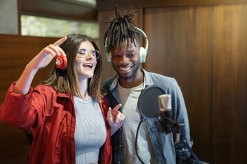 Excited multiethnic couple with microphone and headphones of young broadcasters singing music live and having fun online - Social network content creators duet - people, technology lifestyle concept
