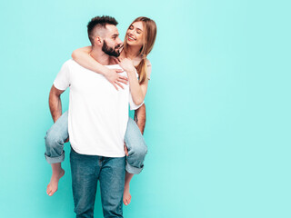 Sexy smiling beautiful woman and her handsome boyfriend. Happy cheerful family having tender moments near blue wall in studio.Pure cheerful models hugging.Gives piggyback riding. Sitting on back