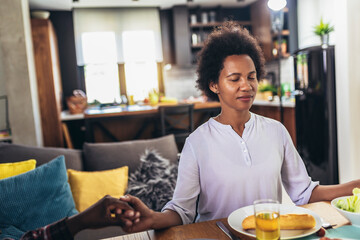 A multi-generational African-American family saying grace at dinner table and holding hands
