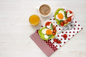 Festive breakfast on Valentine's Day. Two heart-shaped plates with fried eggs, tomatoes and cheese, coffee and juice on a white wooden table. View from above. Banner. Healthy breakfast.