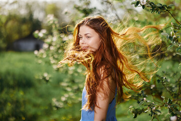 Naklejka premium Woman with a beautiful smile with teeth and long hair flying hair in the spring sunset in nature in the park near the flowering trees happiness, natural beauty and hair health