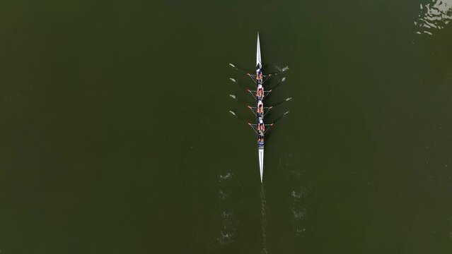 Aerial drone top down view of sport canoe operated by team of young trained sailing along a calm river with the sun reflected in the water. Team of rowers rowing in a boat on a river, sea or lake
