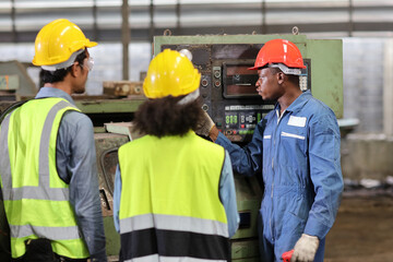 Technician engineer in protective uniform with hardhat standing and teaching apprentices or colleague worker to use computerized machine control at heavy industry manufacturing factory