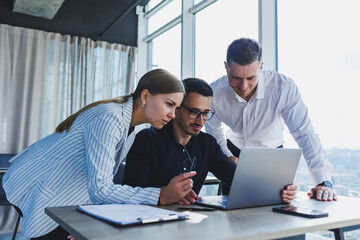 Obraz premium A team of businessmen in formal wear discussing project details and looking at laptop screen while collaborating during a meeting in a modern boardroom. Modern office