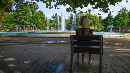 Femme blonde de dos assise devant des jets d'eau