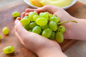 a woman's hand with green grapes, plate of melon slices on a wooden background, concept of fresh sweet fruits and healthy food
